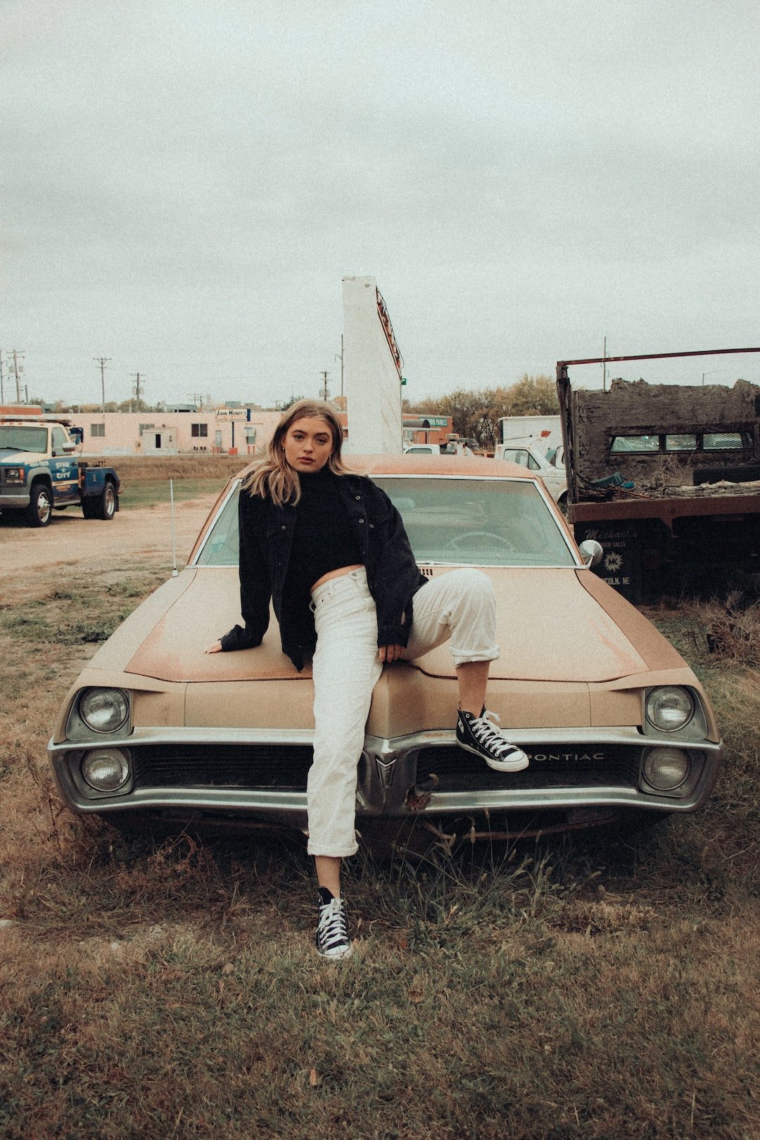 woman in black shirt and white pants sitting on beige car